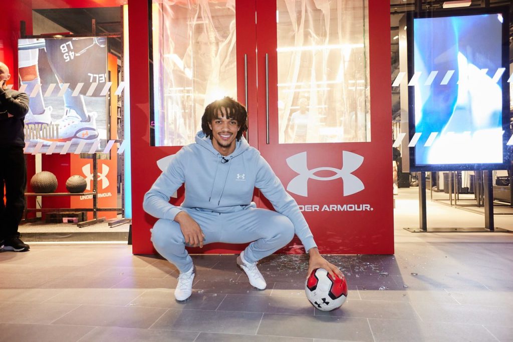 Image of a man holding a ball in front of an Under Armour sign